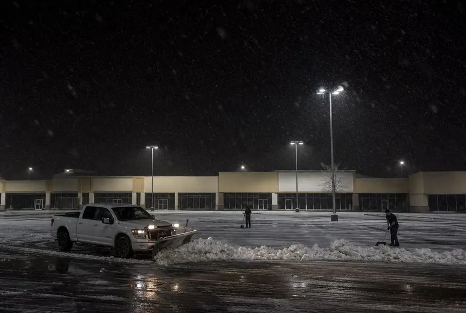 Plow truck clearing an empty strip mall parking lot at night