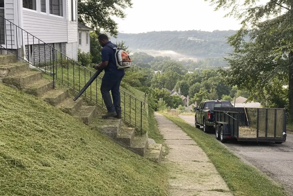 Worker blowing clippings off the front steps of a hillside home