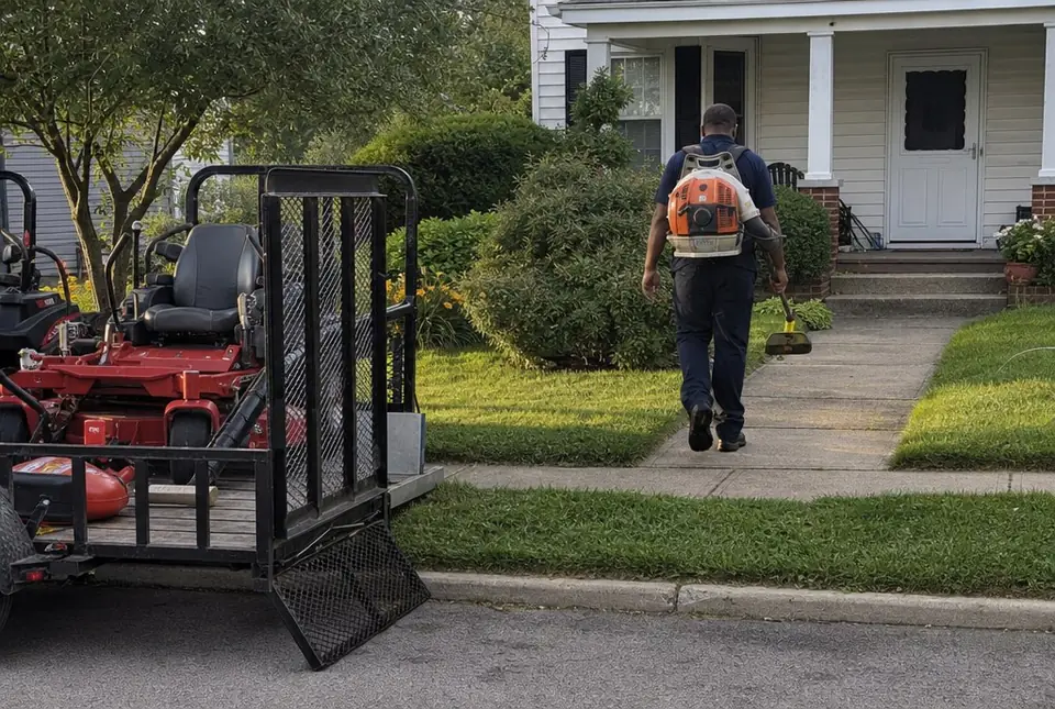Worker carrying a trimmer and blower up a front walk
