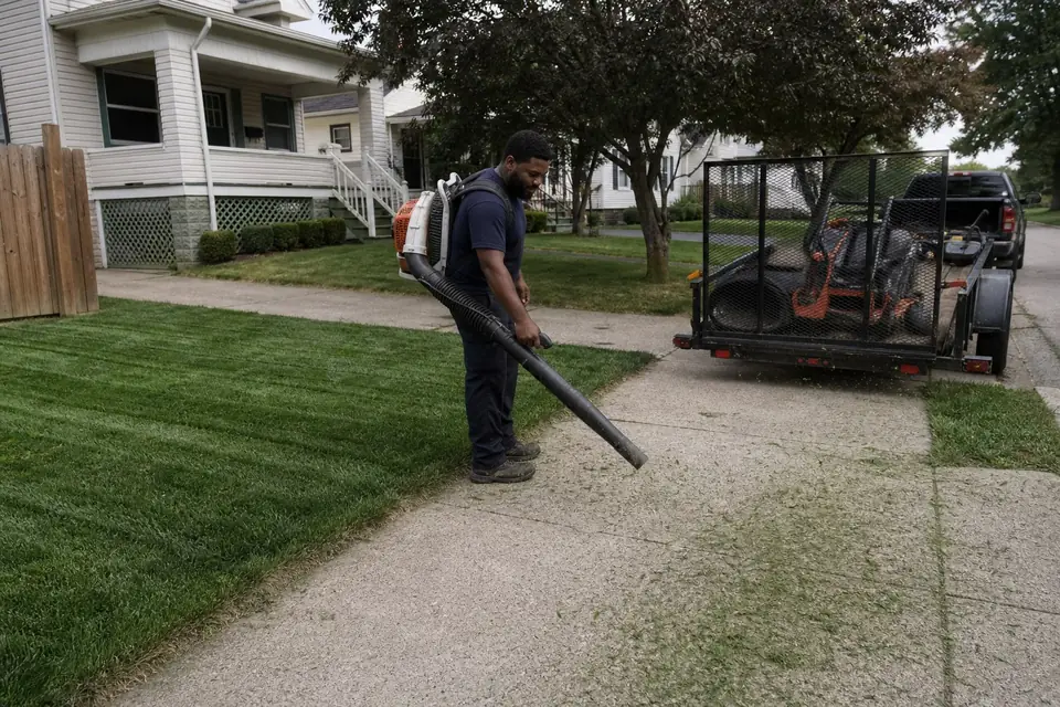 Crew member blowing clippings off a driveway after mowing