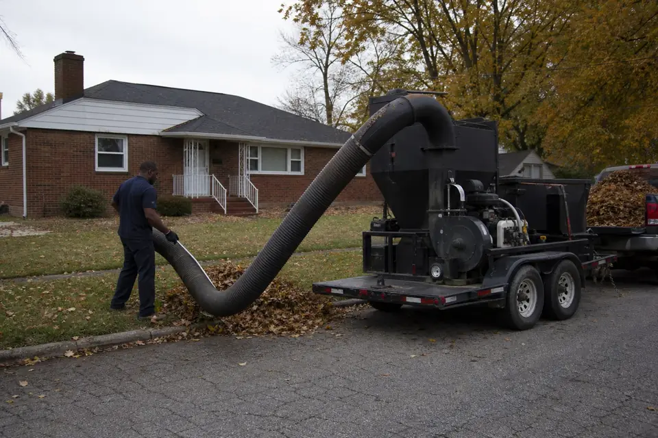 Crew member vacuuming a curbside leaf pile with a trailer leaf loader