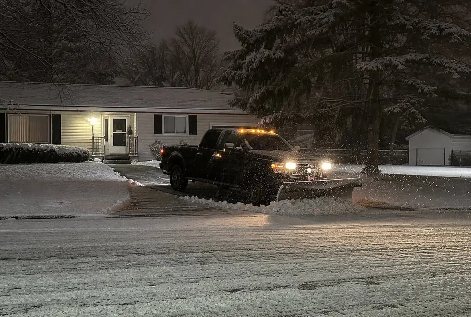 Plow truck clearing a home driveway at night in falling snow